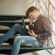 Image of a teen boy sitting on the stairs a looking worrying at his laptop