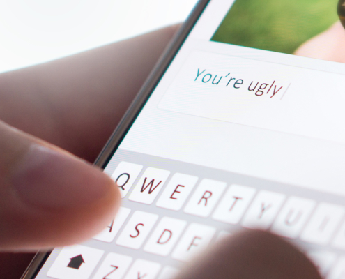 Image of hands commenting on someone's picture "You're uugly" on their smartphones and are about the send the message