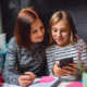 Image of a girl smiling while looking at her smartphone and showing it to her mother