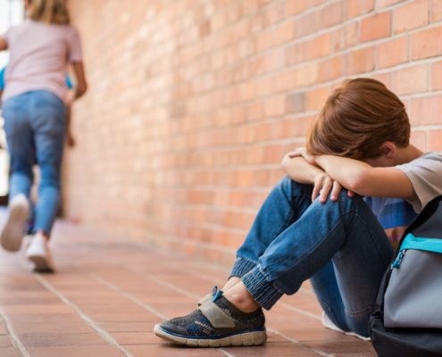 Image of a young boy sitting on the floor and crying with his arms crossed and his head on his arms