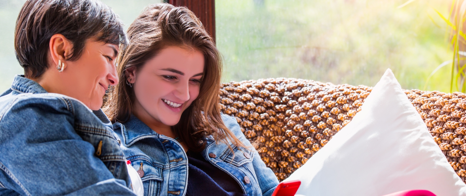 Image of a young teen girl and slightly older woman both looking at the teens smartphone smiling