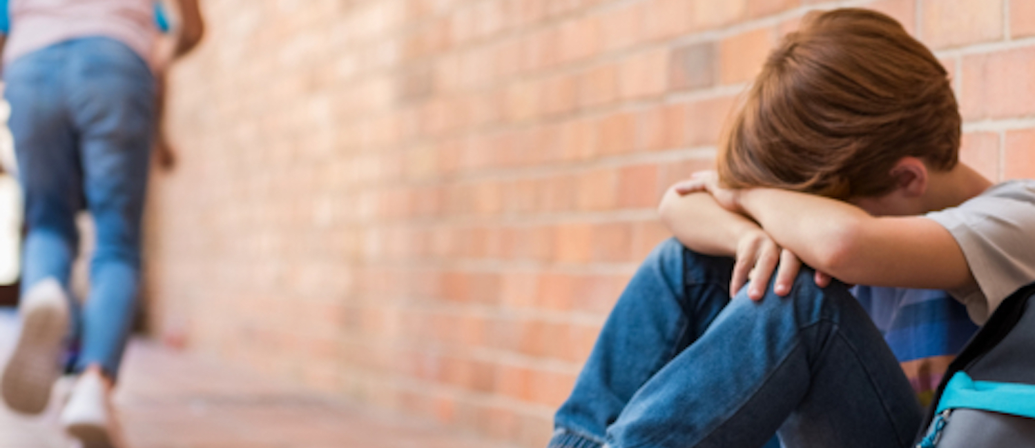 Image of a young boy sitting on the floor and crying with his arms crossed and his head on his arms