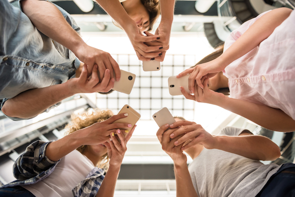 Image shot from below at 5 teens with their smartphones in their hands