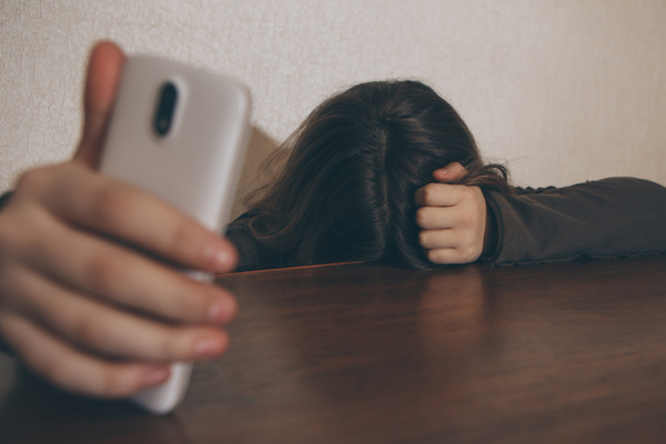Image of a girl hiding behind the desk with a mobile phone in her right hand